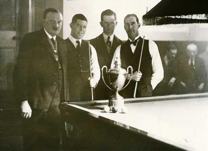 A photograph taken prior to the start of the billiards match at Wolverhampton on 16 February, 1931. Left to right: The Mayor of Wolverhampton (Councillor J. Haddock), Walter Lindrum, the referee Arthur Goundrill, and Clark McConachy. In the centre is the gold cup which Lindrum had recently won with a dramatic comeback in the final against Tom Newman, after conceding 7,000 points start to his 3 opponents in the International Gold Cup Tourney. It was during this match that Lindrum failed to appear at the afternoon session on 19 February. Lindrum had secretly travelled to London by train for a Command Performance at Buckingham Palace.